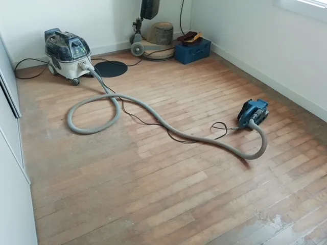 Parquet terne en cours de ponçage, ponceuse et aspirateur dans la pièce