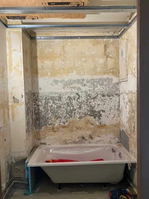 Salle de bains avant travaux : murs décollés et abîmés autour de la baignoire
